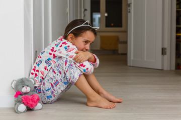Sad little girl sitting near the wall