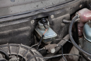 Tank brake cylinder stained with oil with a level sensor and wires electricians in the engine compartment of the car in the workshop for repair and maintenance of vehicles. Auto service industry.