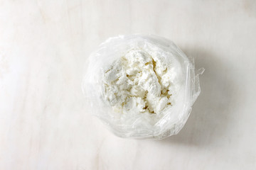 Fototapeta na wymiar Fresh organic cottage cheese in opened plastic bag over white marble background. Flat lay, copy space