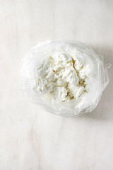 Fresh organic cottage cheese in opened plastic bag over white marble background. Flat lay, copy space