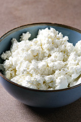 Fresh organic cottage cheese in blue ceramic bowl on brown texture background.Close up, space