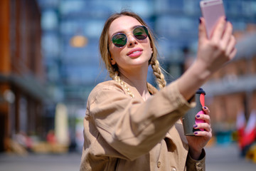 Obraz premium Young happy lady in a spring vacation, walking in the city, drinking coffee, photographing herself on a sunny day