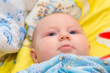 Newborn baby is lying in the baby bed on a yellow background and smiling, close-up.