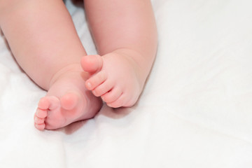 Fototapeta na wymiar Feet newborn baby on a white bedspread. Small baby legs close up.