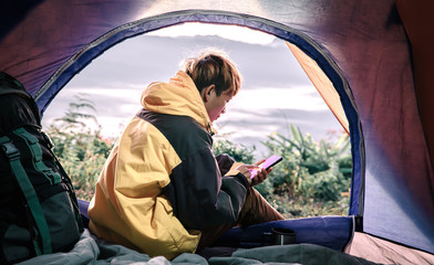 Young male hiker using mobile phone inside a tent in morning enjoying the leisure and freedom.