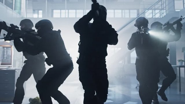 Masked Fireteam of Armed SWAT Police Officers Storm a Bright Seized Office Building with Desks and Computers. Soldiers with Rifles and Flashlights Move Forwards and Cover Surroundings.