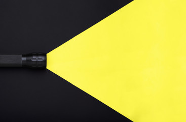 Flashlight turned on with yellow beam light on black background with empty place for text. Top view. Minimal creative concept.