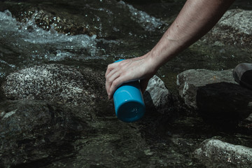 unrecognizable man filling metallic bottle with water from a stream