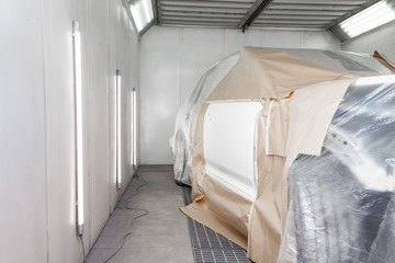 Fototapeta na wymiar A large white car is completely covered in paper and adhesive tape to protect against splash during painting and repair after an accident in a workshop for body repair of vehicles with bright lighting