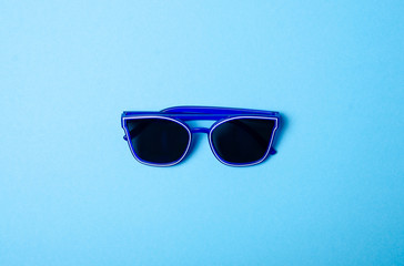 Blue sunglasses fashion on color blue background, top view