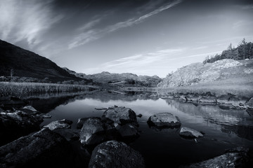 The lake Llynnau Mymbyr reflecting the surrounding landscape of mountains, reeds and rocks.