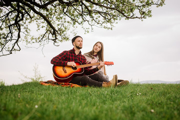 Young couple sitting under the big tree and man playing on the guitar