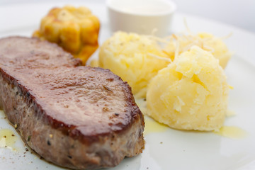 yorkshire pudding and roast beef with mashed potatoes and sour cream sauce on a white plate