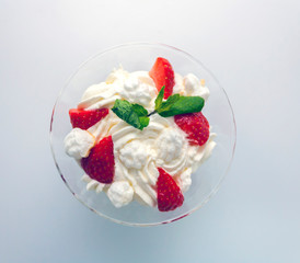 juicy strawberries with cream in a transparent glass bowl on a white background top view