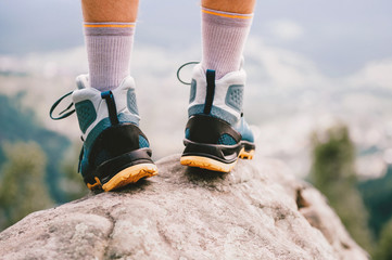 Mood photo of male legs wearing sportive hiking shoes with strong protective sole. Mens legs in trekking footwear for mountain travel standing on stone outdoor at nature on abstract background.