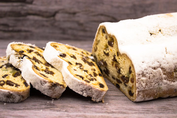 The three slices and the main part of Stollen on a wooden background. Traditional German Christmas cake with marzipan and dried fruits.
