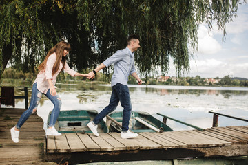 Totally in love. Happy young couple outdoors. young love couple running along a wooden bridge holding hands. love story at the lake