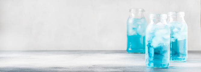Summer refreshing cold drink, isotonic blue water in bottles, gray table background, selective focus
