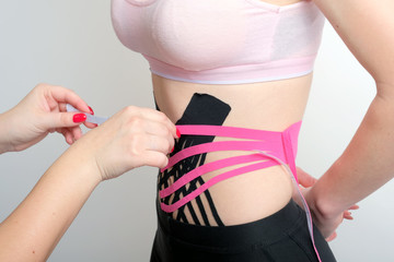 pink and black kinesiology tape on the abdomen of young girl and physiotherapist's hands