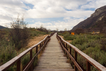 Fototapeta na wymiar Wooden walkway in Lapataia bay, Tierra del Fuego national park, in a winter cloudy day, surrounded by nature and mountains in autumn colors