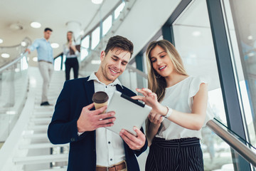 Beautiful business woman and man their holding a tablet in hands and smiling at the camera. In the background are business people.