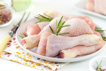 Fresh raw chicken drumsticks on a plate with sprigs of rosemary ready to be cooked