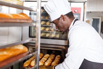 Baker checking readiness of baguettes in bread oven