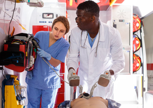 professional afro paramedical using defibrillator for providing medical care to patient