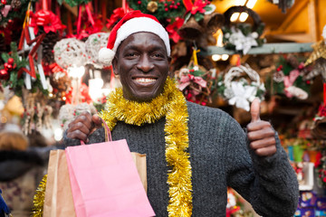 Happy man in Santa hat with bags on Christmas market