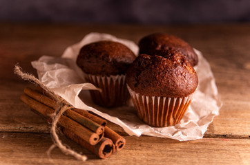 Fresh chocolate muffins and cinnamon sticks on rustic wooden background