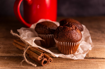 Fresh chocolate muffins and cinnamon sticks on rustic wooden background