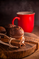 Fresh chocolate muffins and cinnamon sticks on rustic wooden background