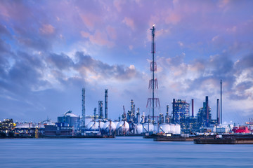 Obraz premium Riverbank with petrochemical production plant against a dramatic blue sky at twilight, Port of Antwerp, Belgium.