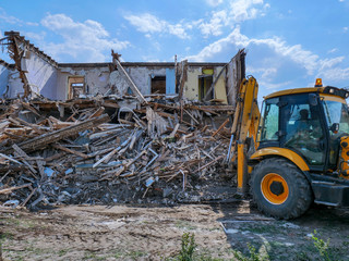 Destruction of walls of old building and cleaning of construction debris with bucket of excavator..bulldozer demolishing concrete brick walls of small building