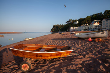 An empty beach with a wooden row boat sitting on a trailer on a sunny evening