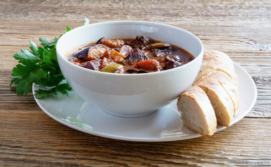 braised veal, olives, eggplant, and tomatoes stewed in red  wine served  with bread and parsley on wooden surface