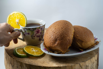 two brown breads on a plate and one cup of warm lemon tea are placed on a wooden mat with an isolated white background
