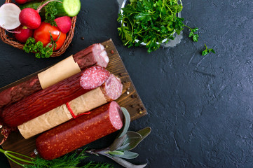 Several kinds of sausage, fresh vegetables and greens on a black background. Products to the holiday.