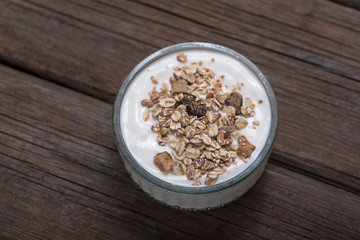 Glass bowl with white yogurt on old wooden desk with oatmeal on top.