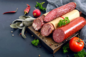 Several kinds of sausage, fresh vegetables and greens on a black background. Products to the holiday.