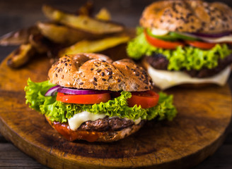 Home made hamburger with green salad and with american potatoes behind. Brown wooden background.Home made hamburger with green salad and with american potatoes behind. Brown wooden background.