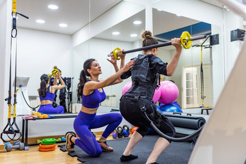 EMS electro stimulation women exercises with trainer coach.  Female athlete wearing ems workout top and strapped to heart monitors.  Exercising in fitness studio and wearing ems outfits