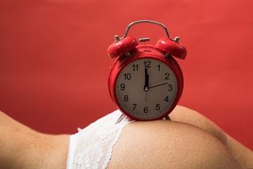 Sexy time, retro alarm clock on female ass. Beautiful naked female body with big clock on red background. Buttocks and age concept.