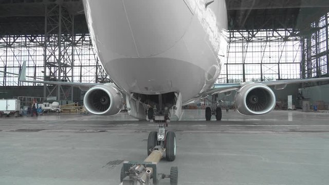 Pushback of a passenger aircraft at the airport in hangar. The airplane nose, landing gear and towing truck close up. 4k