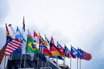 Waving flags of almost all countries on flagpoles on the top of the dutch house roof  