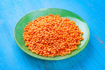 Red lentils in a green plate on a blue wooden background.