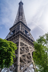 Eifel Tower full length bottom up low angle shot from tower basement with blue sky cloudy background and two green trees  