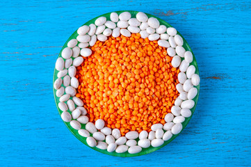 Top view red lentils and white beans in a green plate on a blue wooden background.