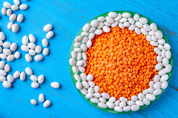 Top view white beans and red lentils in a green plate on a blue wooden background.