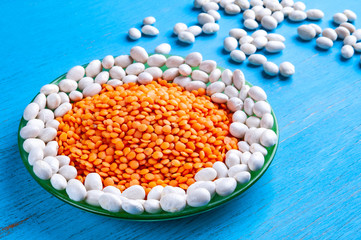 Red lentils and white beans in a green plate on a blue wooden background.